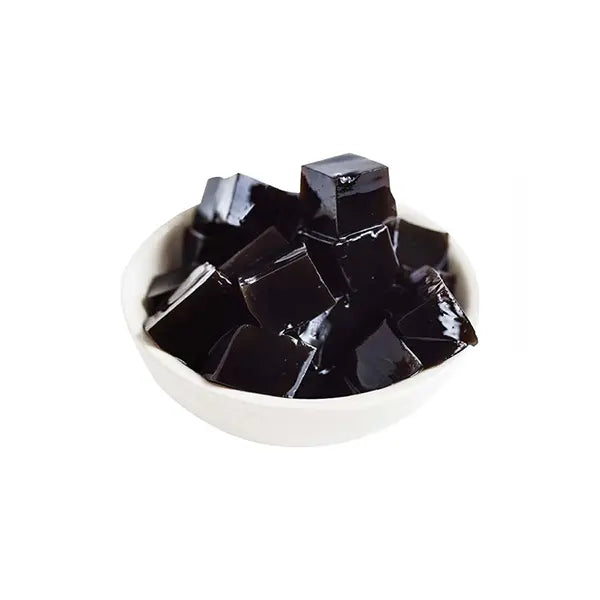 Cooked grass jelly cubes in a white bowl, glossy and soft texture, ready to serve with drinks or desserts.