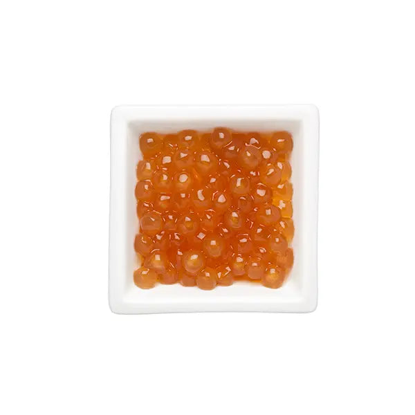 Golden tapioca pearls in a white dish, showcasing their vibrant amber color and glossy texture for milk tea and desserts.