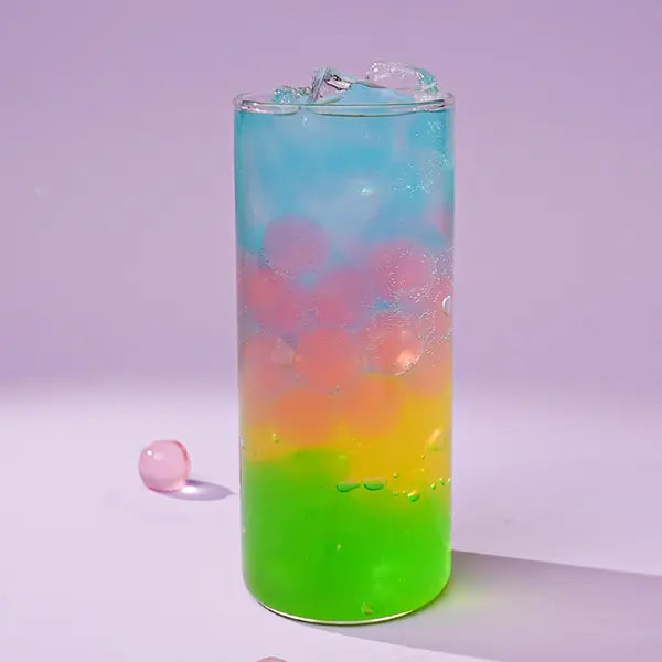 Colorful layered iced drink with green apple syrup base, blue top layer, and pink popping boba, served in a tall glass with ice.